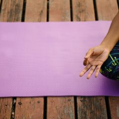 A lilac yoga mat on a wooden deck with a hand resting on it