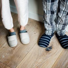 Two pairs of slippers on a wooden floor, one navy and white striped, with pyjama trousers