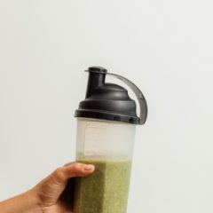 A hand holding a clear shaker bottle with a black flip-top lid and carry loop