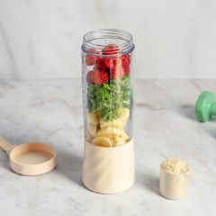 Personal blender with a tall cup of strawberries, spinach and banana on a cream base, on a marble worktop