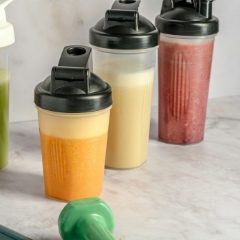 Clear shaker bottles with black flip-top lids holding fruit shakes on a marble worktop