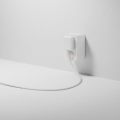 A small white smart plug in a wall socket with a lamp lead plugged in