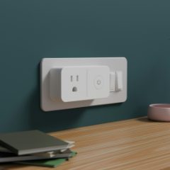 A white smart plug with a power button in a wall socket above a wooden shelf
