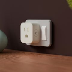 A square white smart plug with a power button in a wall socket beside vases
