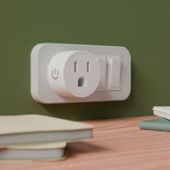 A round white smart plug with a power button on a sage green wall