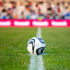 White football with black swirls on the halfway line of a stadium pitch