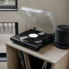 A black turntable with its lid up on a wooden record cabinet