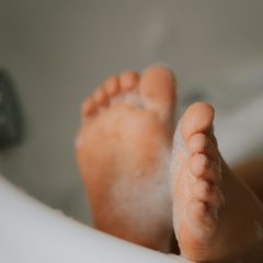 Close-up of the soles of two bare feet with soap suds in a white bathtub