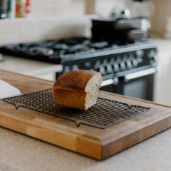 Freshly baked loaf cooling on a wire rack on a wooden board in a bright kitchen, a black range cooker behind