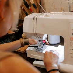 Woman sewing at a white computerised sewing machine with buttons and a small display in a warm workshop