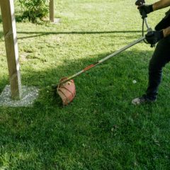 A grass trimmer with an orange guard cutting the lawn beside a post