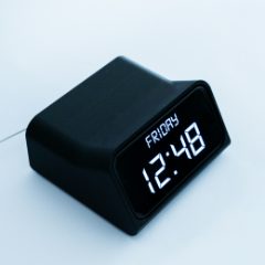 A black digital alarm clock with bright white numbers showing the day and time