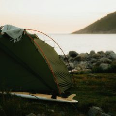 An olive green dome tent pitched by a rocky shore at sunset