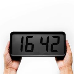 Two hands holding a black digital clock with a large grey display on white