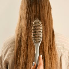 Hand drawing a pale grey open-vented oval brush down long straight brown hair