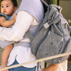 A parent carrying a baby in a sling with a grey backpack on