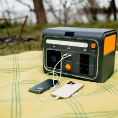 A black and orange power station charging two phones on a picnic blanket