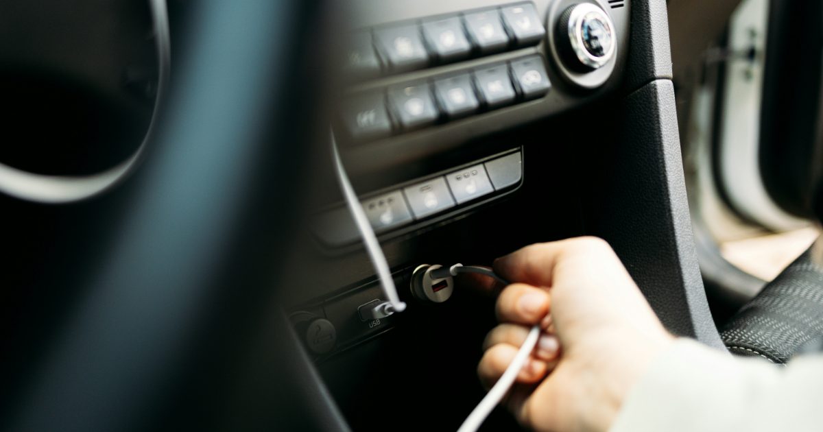 Hand plugging a white USB cable into a small round car charger in the dashboard socket