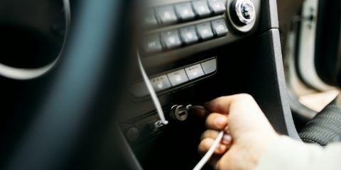 Hand plugging a white USB cable into a small round car charger in the dashboard socket