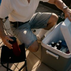 A man packing a grey cool box with bottles