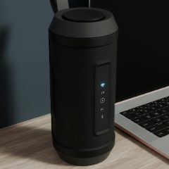 Black cylindrical portable speaker standing on a wooden desk beside a laptop