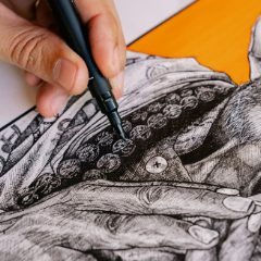A hand inking fine detail with a black fineliner