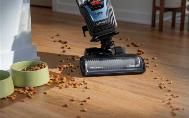 Bissell Pet Hair Eraser Allergen Lift-Off vacuum cleaning spilled kibble beside two pet bowls on a sunlit wood floor