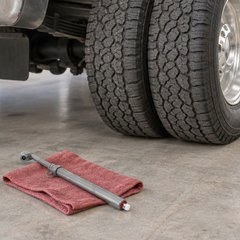 Brass dual-head stick tire gauge on a shop rag beside a truck’s dual rear wheels