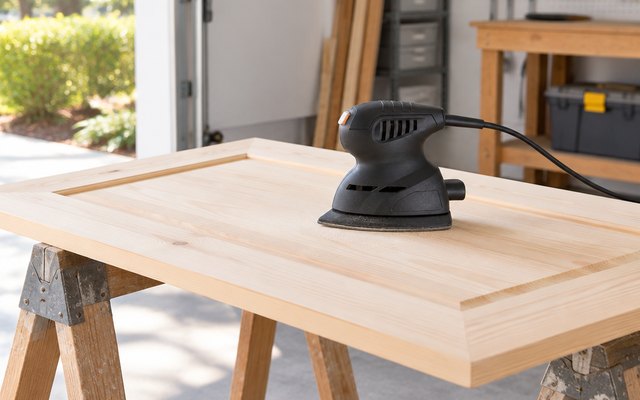 WEN 6301 detail sander, sitting on a flat pine cabinet door laid across two sawhorses in a bright garage