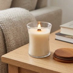 Lit hourglass candle of cream wax with its wooden lid beside it on an oak side table by a sofa