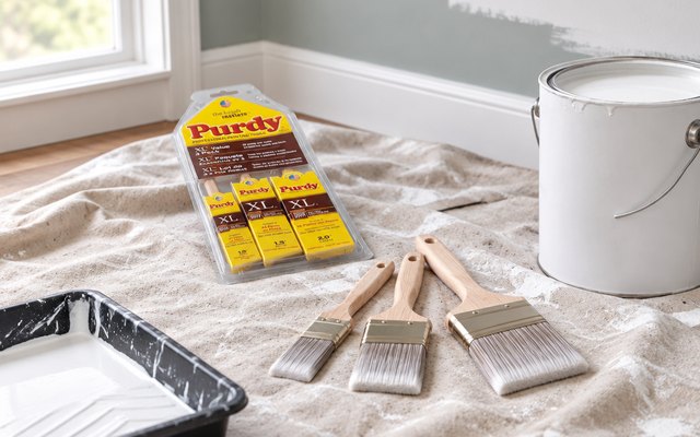 Purdy XL paint brush set, laid on a drop cloth beside an open can of white paint in a room being painted