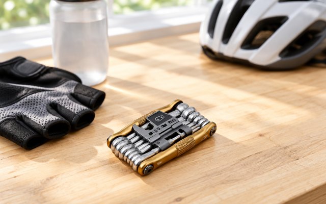 Crankbrothers M19 multi-tool on a wooden workbench beside cycling gloves and a water bottle