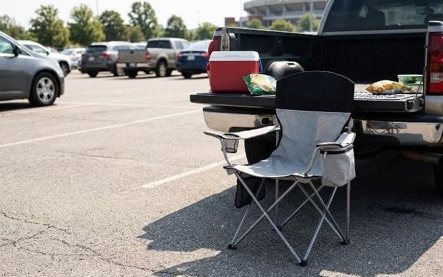Grey and black quad camping chair with a cooler armrest, open beside a pickup’s lowered tailgate