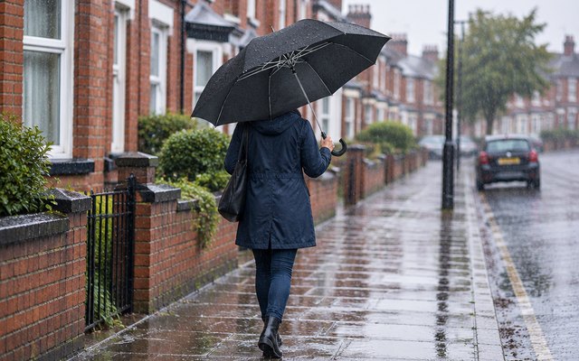 Black umbrella with a crook handle, open on a rainy street of brick terraced houses