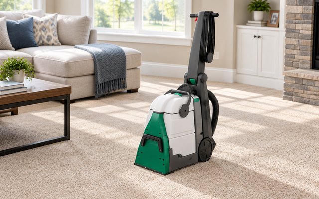 BISSELL Big Green carpet cleaner, standing on a freshly cleaned beige wall-to-wall carpet in a sunny family room with a sectional sofa