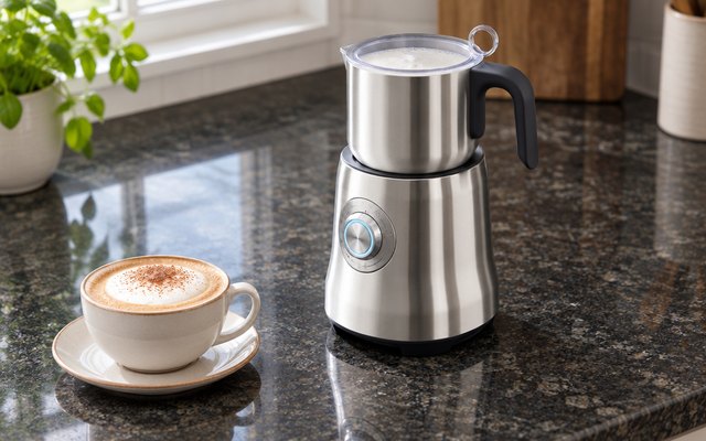 Breville Milk Café frother, on a dark granite kitchen counter beside a cappuccino cup