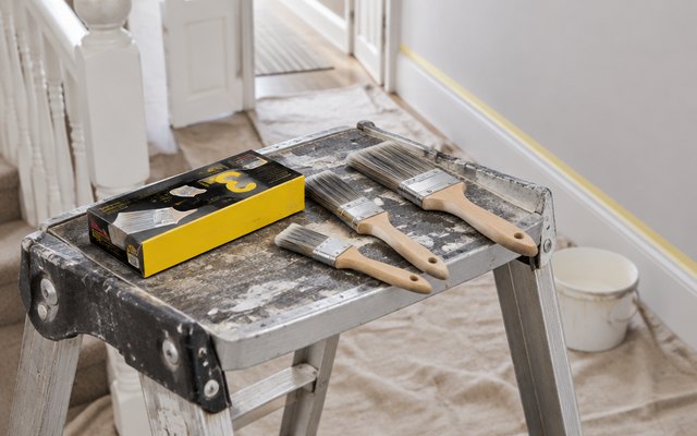 Purdy Monarch Elite brushes, laid on the platform of a stepladder in a hallway being redecorated, masking tape on the skirting board