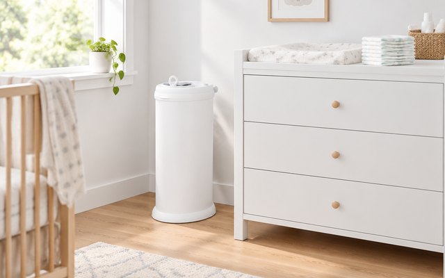 Ubbi Steel Diaper Pail, steel diaper pail beside a white changing table in a bright nursery, a stack of folded diapers on the table