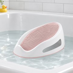 Angelcare Baby Bath Support, resting in a few inches of water in a white bathtub, white subway tile behind and a rubber duck on the ledge