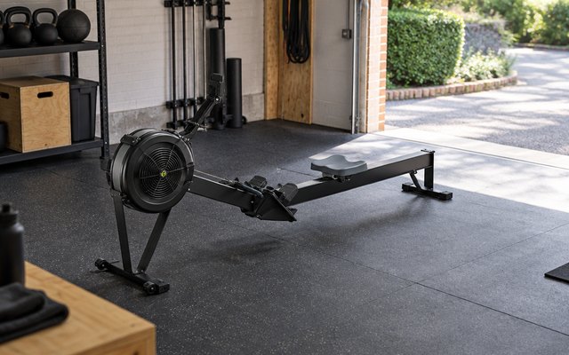 Concept2 RowErg, in a British garage turned home gym, with a rubber floor mat and the garage door open to daylight