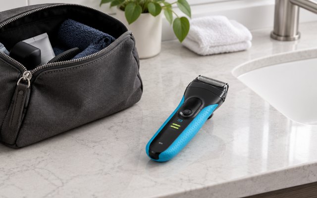 Blue and black foil shaver beside an open toiletry bag on a bathroom counter