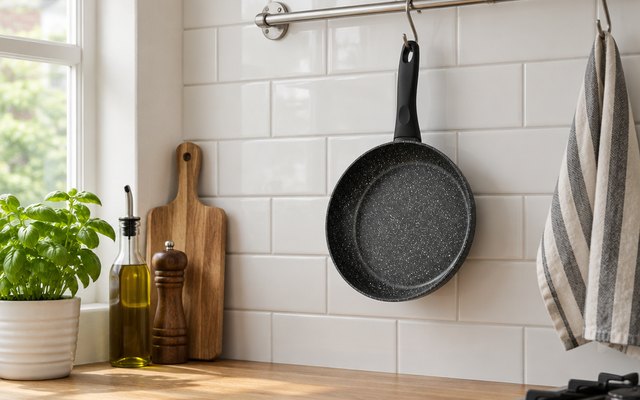Frying pan, hanging from a rail on a tiled wall in a British kitchen