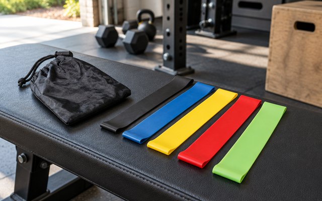 Fit Simplify Resistance Loop Exercise Bands, Set of 5, on a bench in a garage gym, daylight
