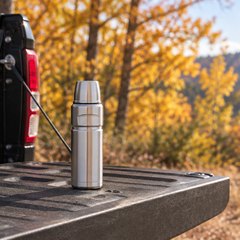 THERMOS Stainless King compact bottle, standing on the tailgate of a pickup truck on a fall morning, golden trees behind
