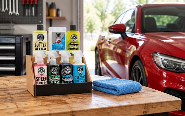 Starter car care kit of bottles and pads, on a garage workbench beside a folded microfiber towel, a glossy red car parked in the bay behind