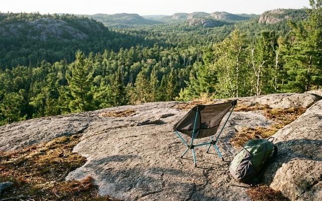 Ultralight black camping chair on a granite rock at a trail lookout above a forested valley