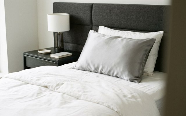Pillow in a silver-grey silk pillowcase on a bed with a charcoal upholstered headboard