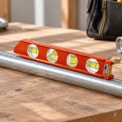 Klein Tools torpedo level, resting on a length of metal conduit on an electrician's workbench