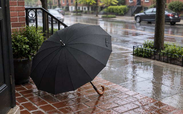 Royal Walk stick umbrella, propped on a brick front stoop on a rainy afternoon, a wet street behind