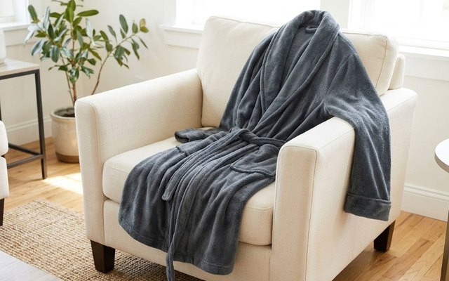 Slate grey plush fleece bathrobe laid over a cream armchair in a bright living room